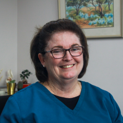Dr Kathleen Mulholland smiles at the camera. She has short dark hair and is wearing dark glasses and a blue scrub top.