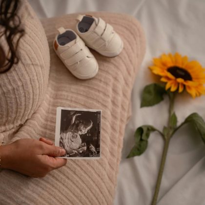 Pregnant Woman Holding Ultrasound with Baby Shoes and Sunflower